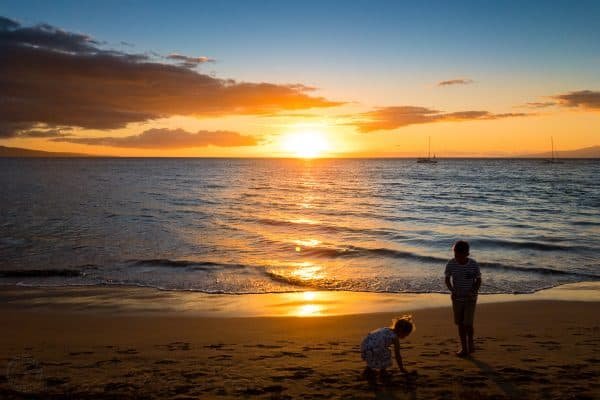 Two children playing at the beach at sunset