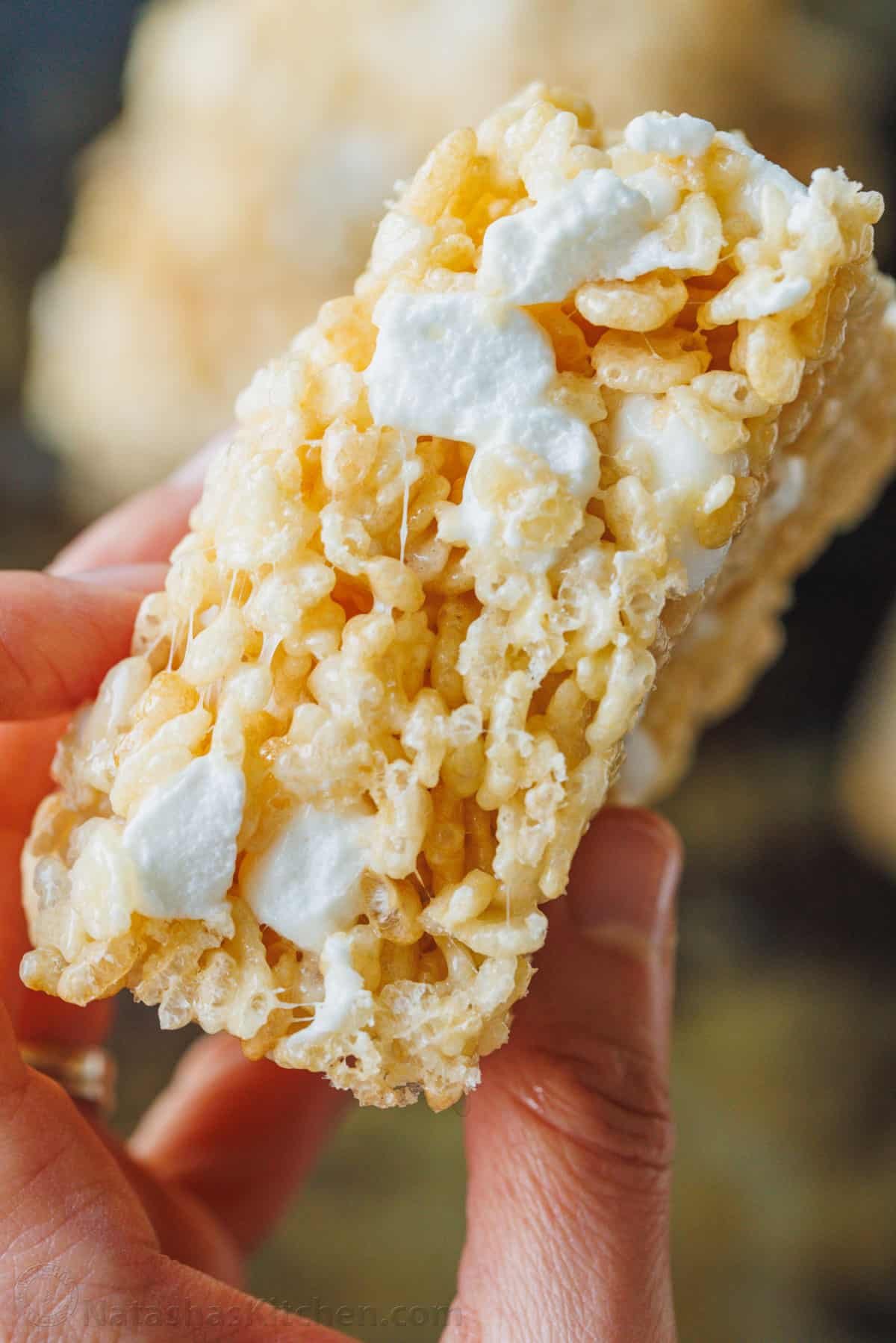 Make thick and gooey Rice Krispie Treats filled with sweet and sticky marshmallows and crispy rice crunch. A family-favorite no-bake dessert! A hand holding a thick homemade Rice Krispie treat.
