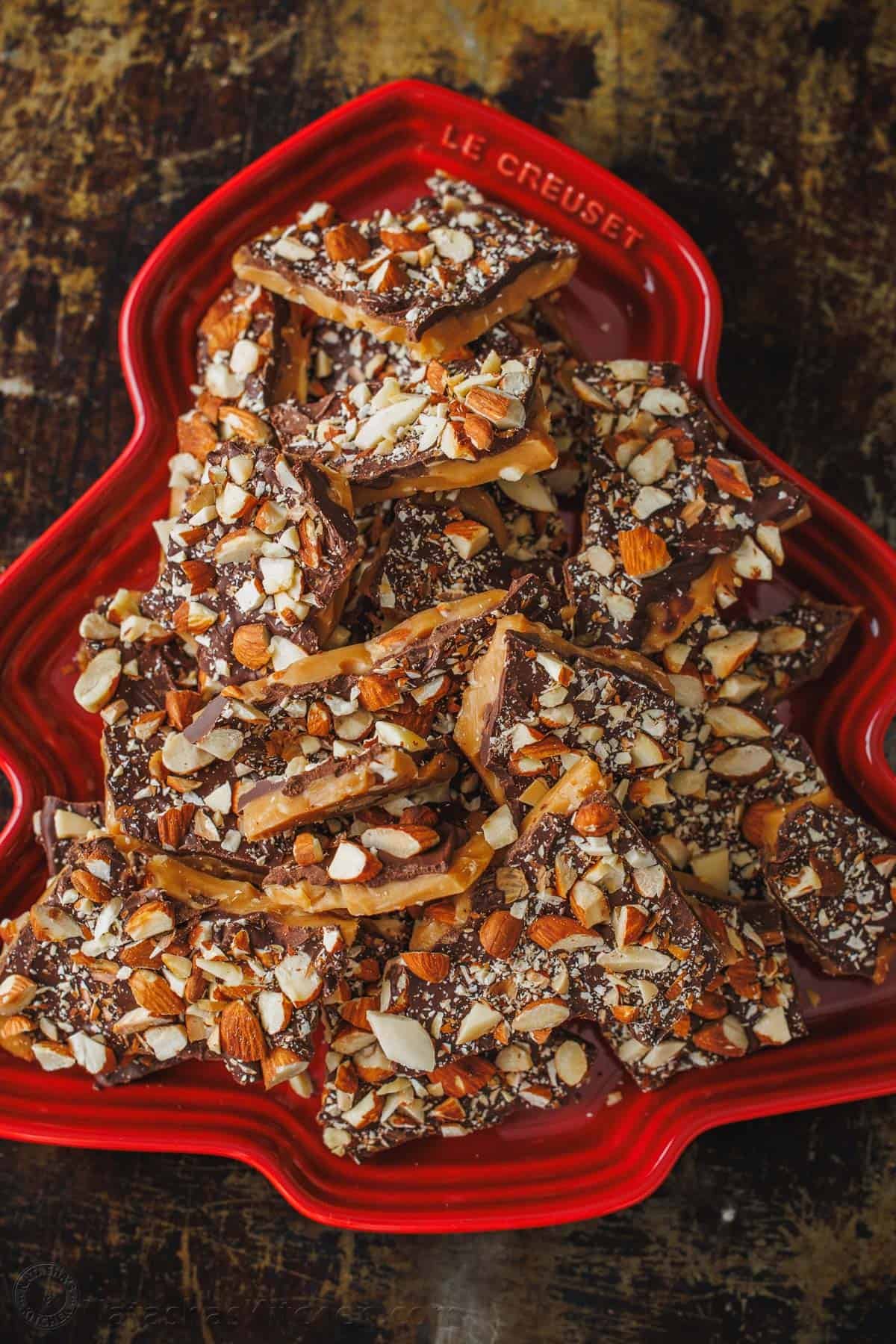 Our toffee recipe is buttery and crunchy with delicious layers of candy, chocolate and almonds. It's easy to make with only 5 ingredients. Chocolate and nuts layered with candy in a red holiday dish