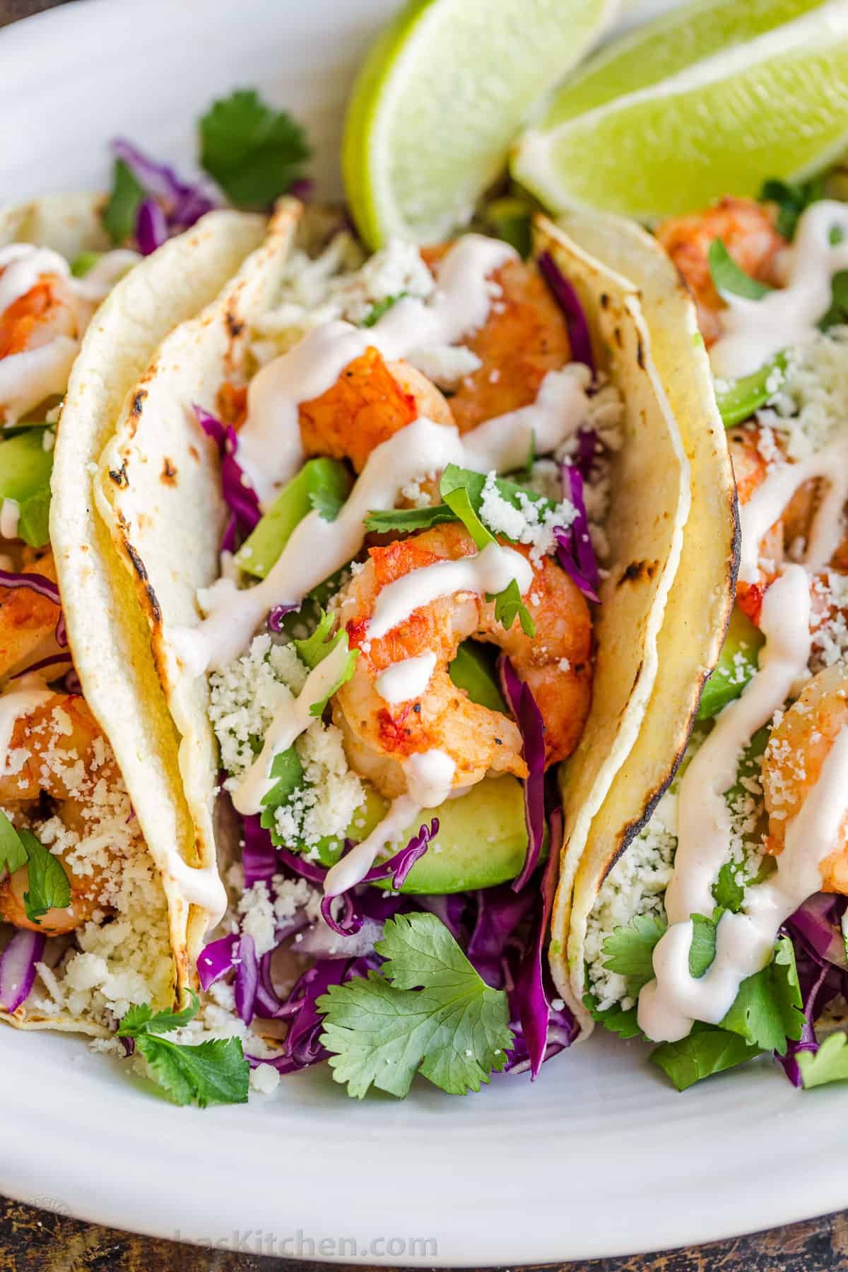 My easy Shrimp Tacos are loaded with shrimp, cabbage slaw, cotija cheese, and the BEST garlic-lime crema sauce. It's the only recipe you need! Shrimp Taco up close with shrimp, avocado, cabbage, cilantro and red onion drizzled with garlic-lime crema shrimp taco sauce
