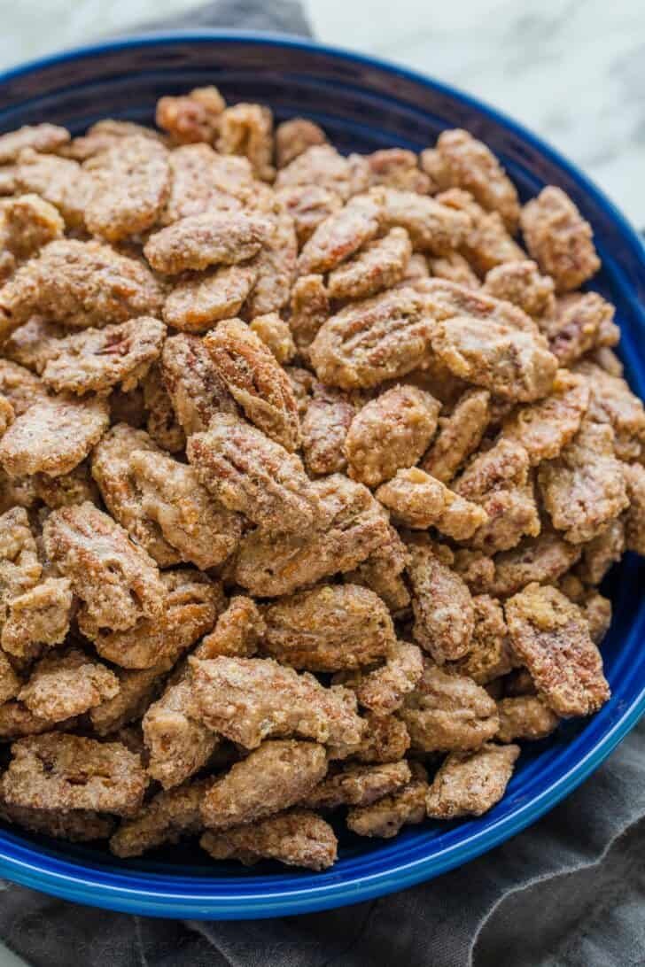 Candied pecans are easy and great for munching, gifting, and topping. The cinnamon sugar caramelizes and gives them a delicate praline crunch Blue bowl filled with praline pecans