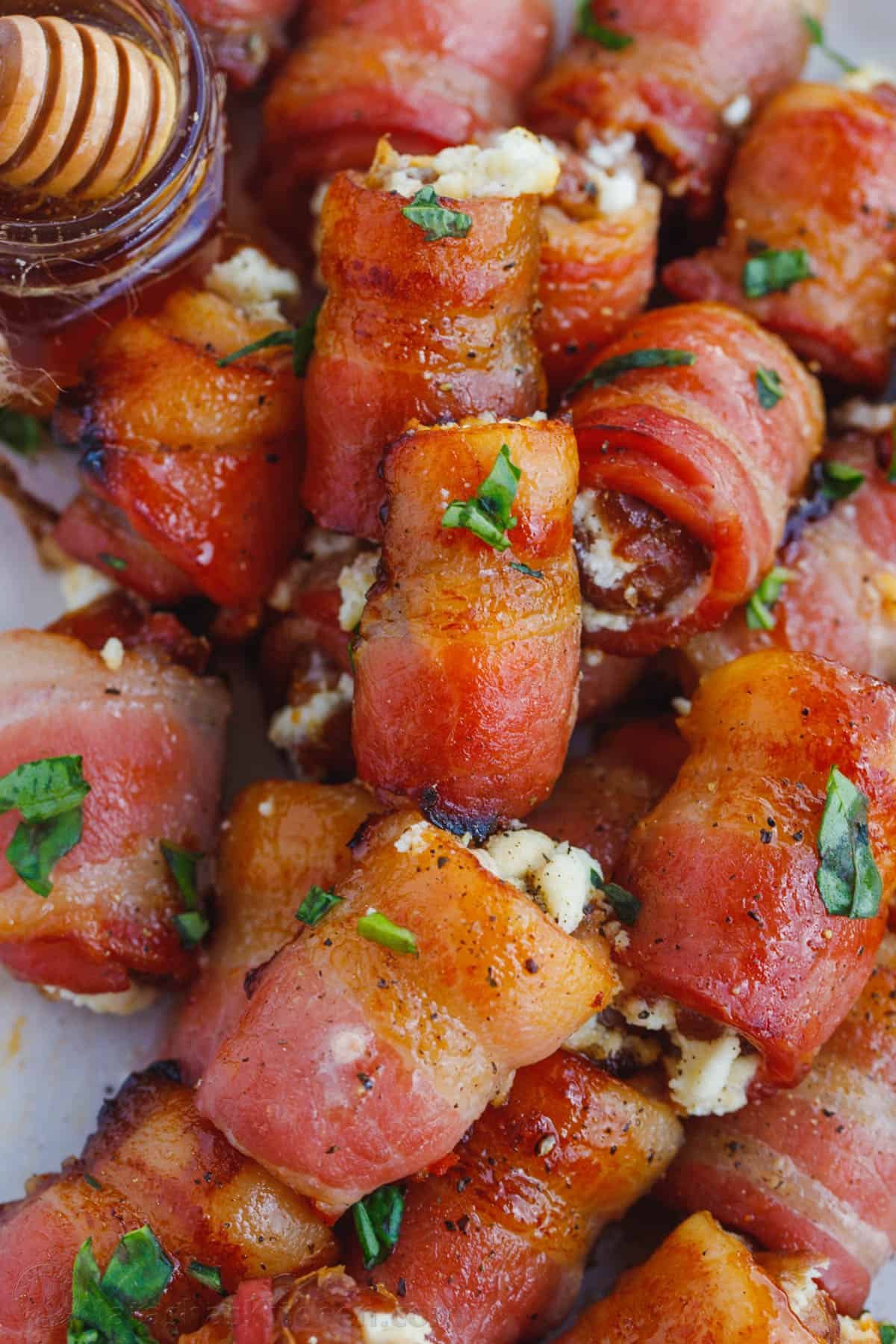 Stuffed dates wrapped with bacon make for the best appetizer and side dish for the holidays and parties. Stuffed Dates on a plate with a jar of honey.