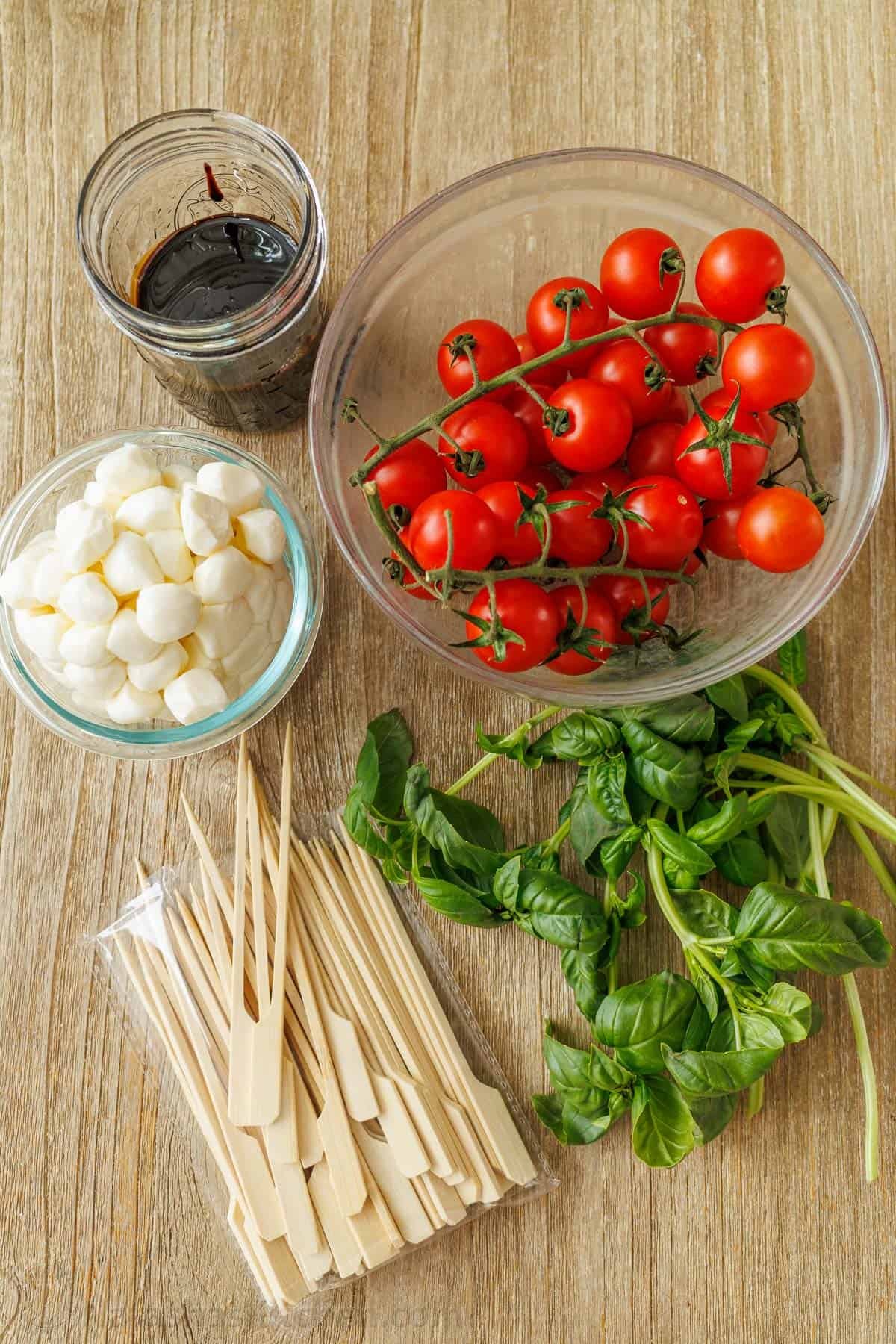 Caprese Skewers is the bite-sized version of the classic Caprese Salad. It takes 10 minutes and 4 ingredients to make these fancy appetizers! ingredients for antipasto salad including balsamic glaze, mozzarella balls, skewers, basil and tomatoes