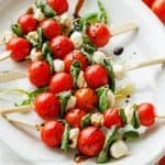 Tomatoes and mozzarella cheese appetizers on a toothpick served lined up on a white plate with balsamic glaze over top