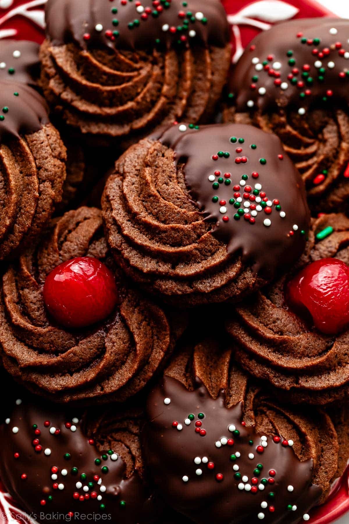 plate of chocolate butter cookies dipped in chocolate with sprinkles and maraschino cherries.