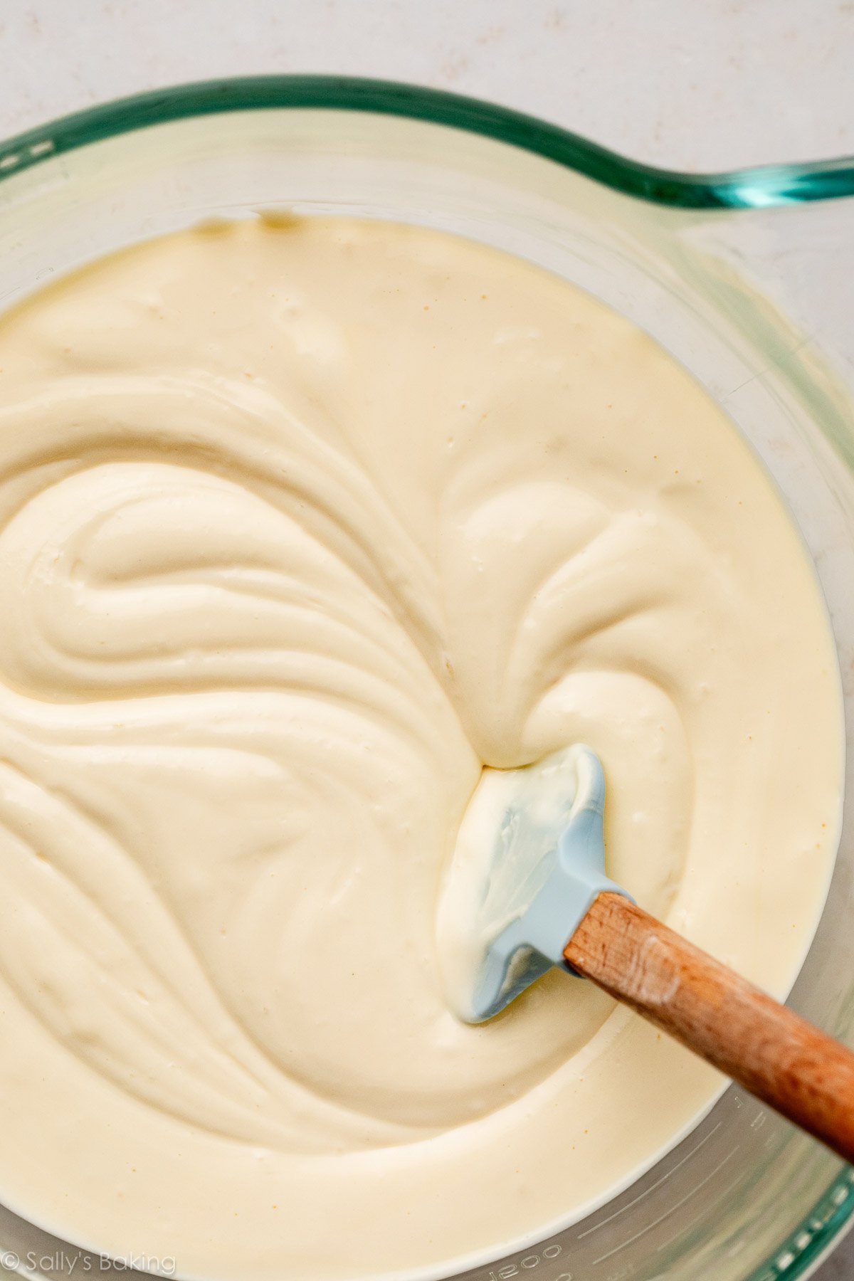 creamy cheesecake batter with blue spatula in glass bowl.