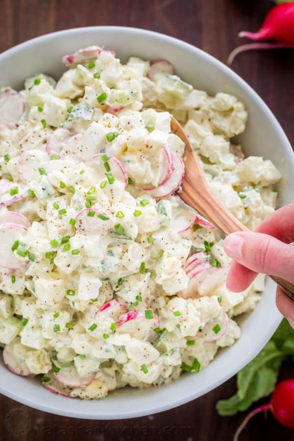 Creamy potato salad served with a spoon and garnished with green onion