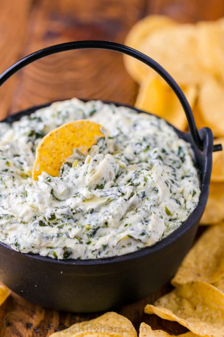 Spinach Artichoke Dip is irresistibly creamy and loaded with spinach and artichokes. This is our go to dip for parties. It's an easy, excellent appetizer! #spinachartichokedip #spinachandartichokedip #spinachdip #artichokedip #dip #appetizer #natashaskitchen Creamy Spinach artichoke dip in serving bowl surrounded by tortilla chips