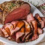 Perfect roast beef sliced thinly on a platter, drizzled with beef gravy.