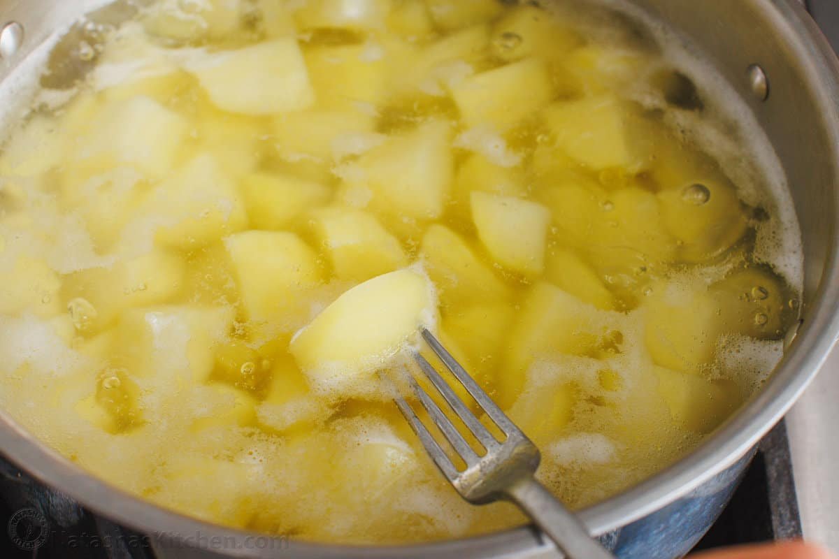 This is a simple sour cream mashed potatoes recipe with loads of buttery flavor. Enjoy homemade mashed potatoes as an easy, versatile side! A fork pierces a piece of boiled potato in a pot filled with water.