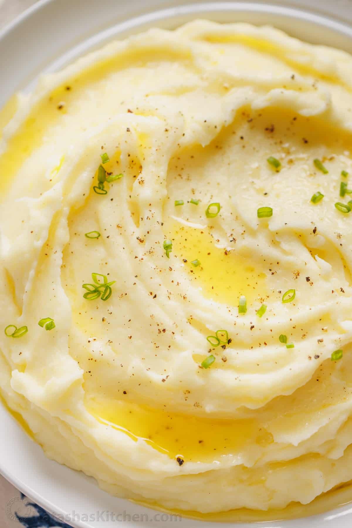 This is a simple sour cream mashed potatoes recipe with loads of buttery flavor. Enjoy homemade mashed potatoes as an easy, versatile side! A bowl of sour cream mashed potatoes topped with melted butter and freshly chopped chives, with a spoon.