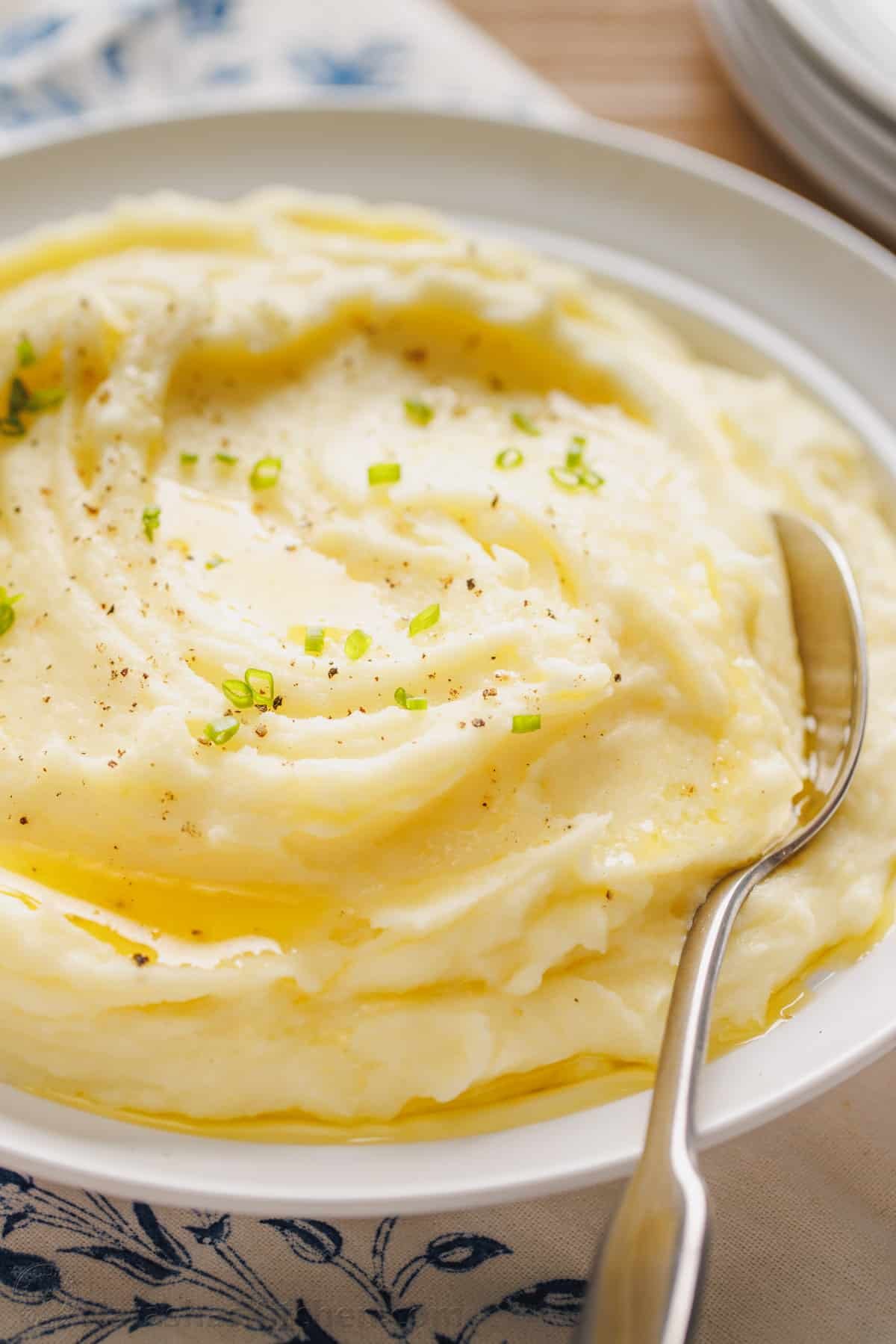 This is a simple sour cream mashed potatoes recipe with loads of buttery flavor. Enjoy homemade mashed potatoes as an easy, versatile side! A bowl of sour cream mashed potatoes topped with melted butter and freshly chopped chives, with a spoon.