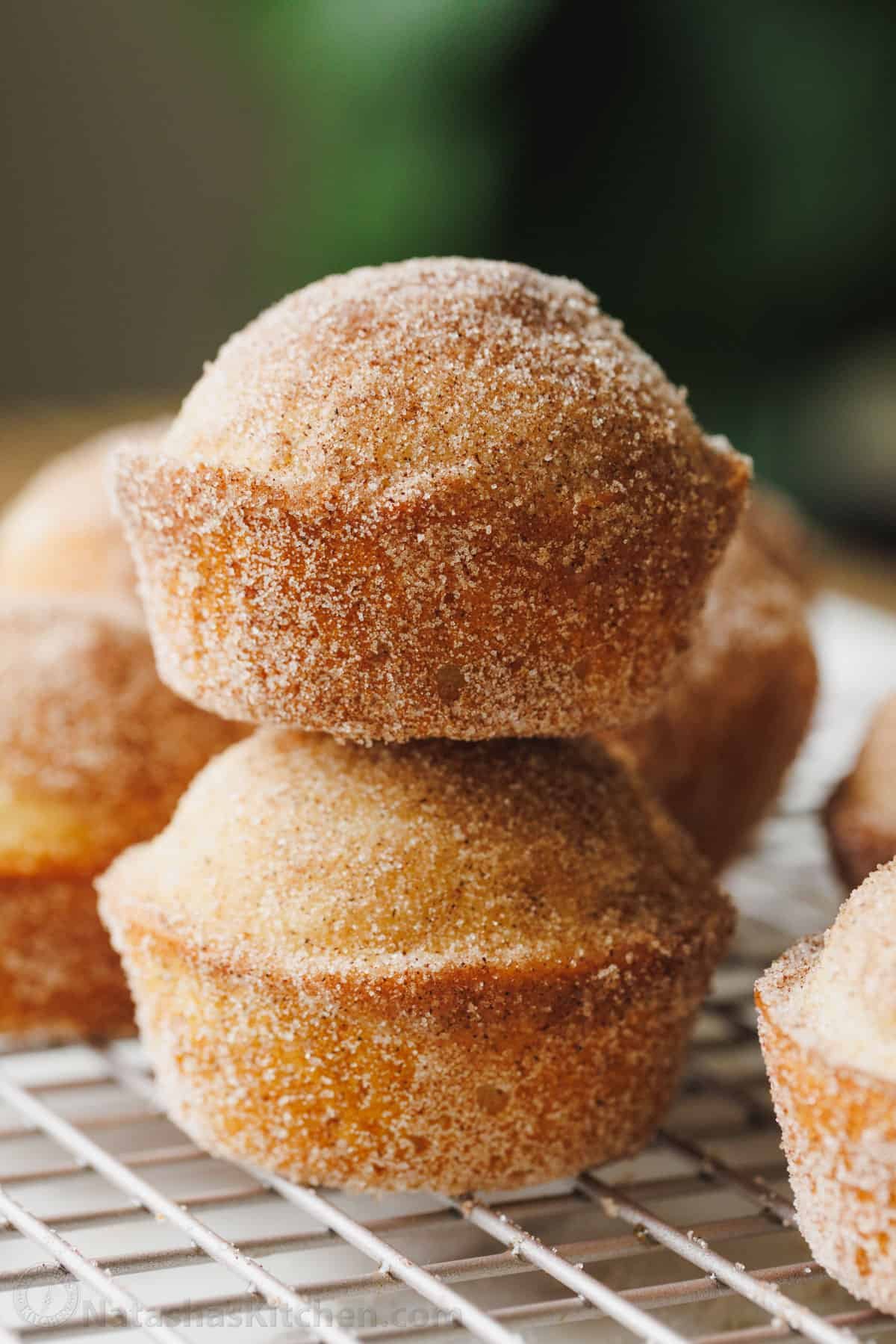 Fluffy cinnamon muffins filled with warm spice and dipped in cinnamon sugar for an irresistible, sugary crunch. Ready in 25 minutes! Two cinnamon muffins stacked on top of one another on a wire rack.