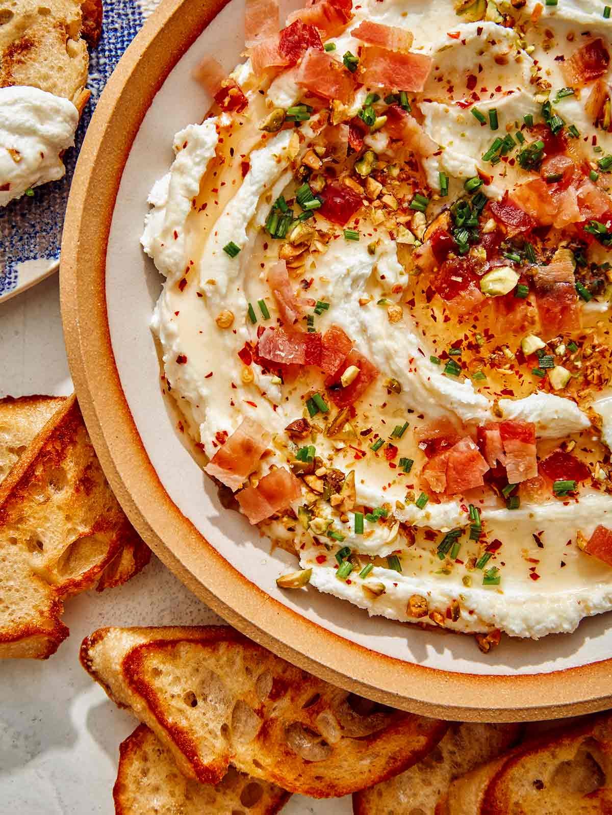 Whipped goat cheese in a bowl with crostini on the side.
