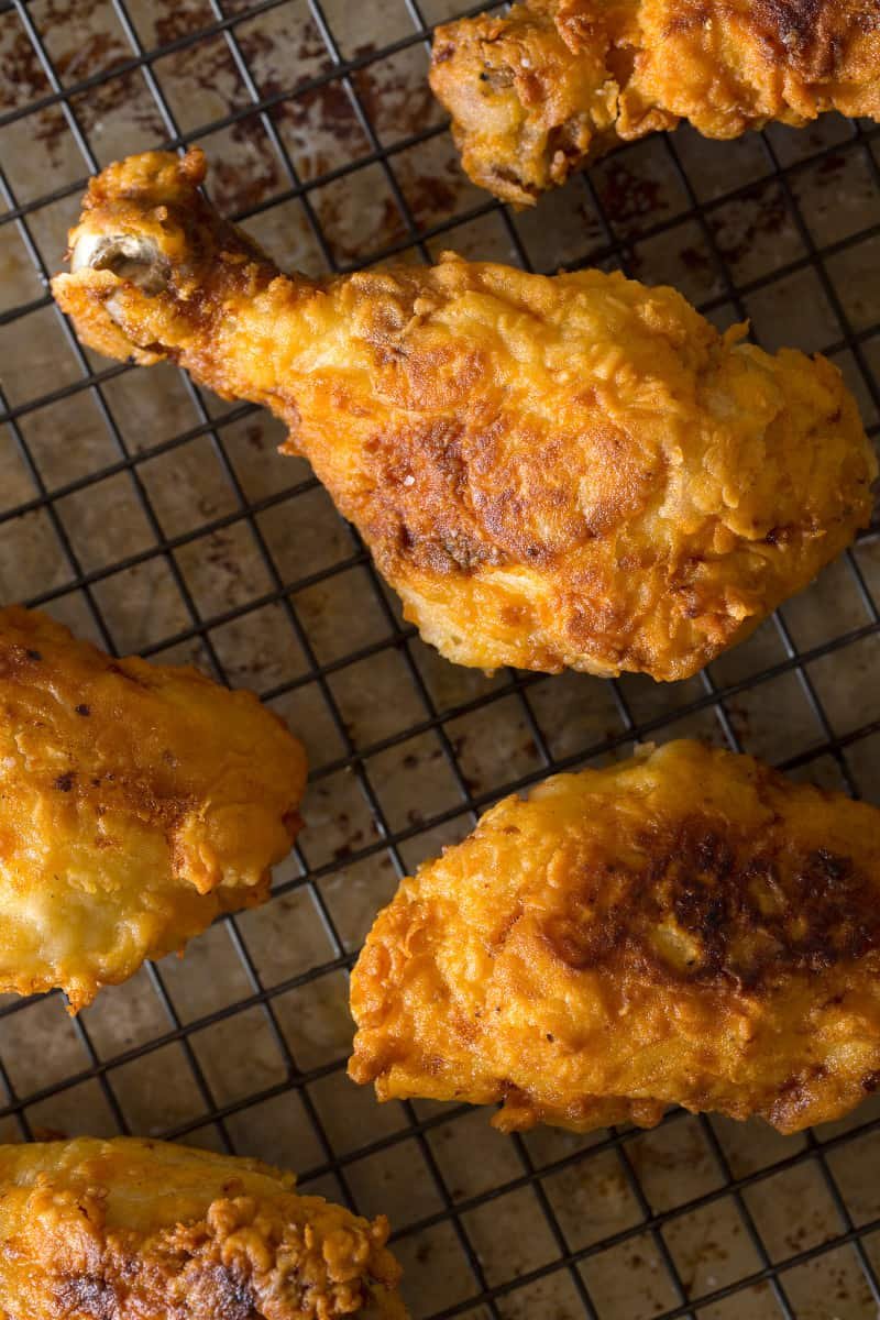 A close up of finished fried chicken drumsticks on a wire rack.