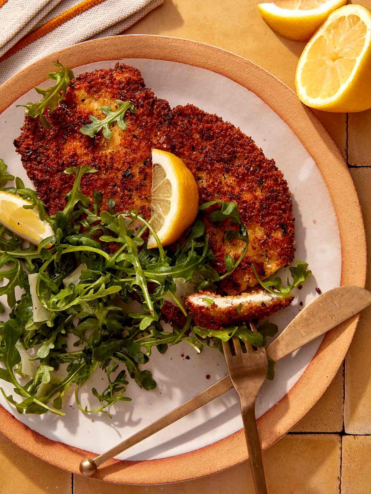 Chicken milanese being cut into on a plate.