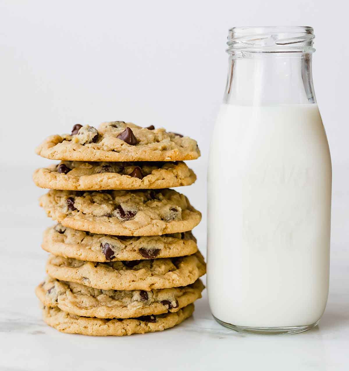 A stack of peanut butter oatmeal chocolate chip cookies next to a jar of milk.