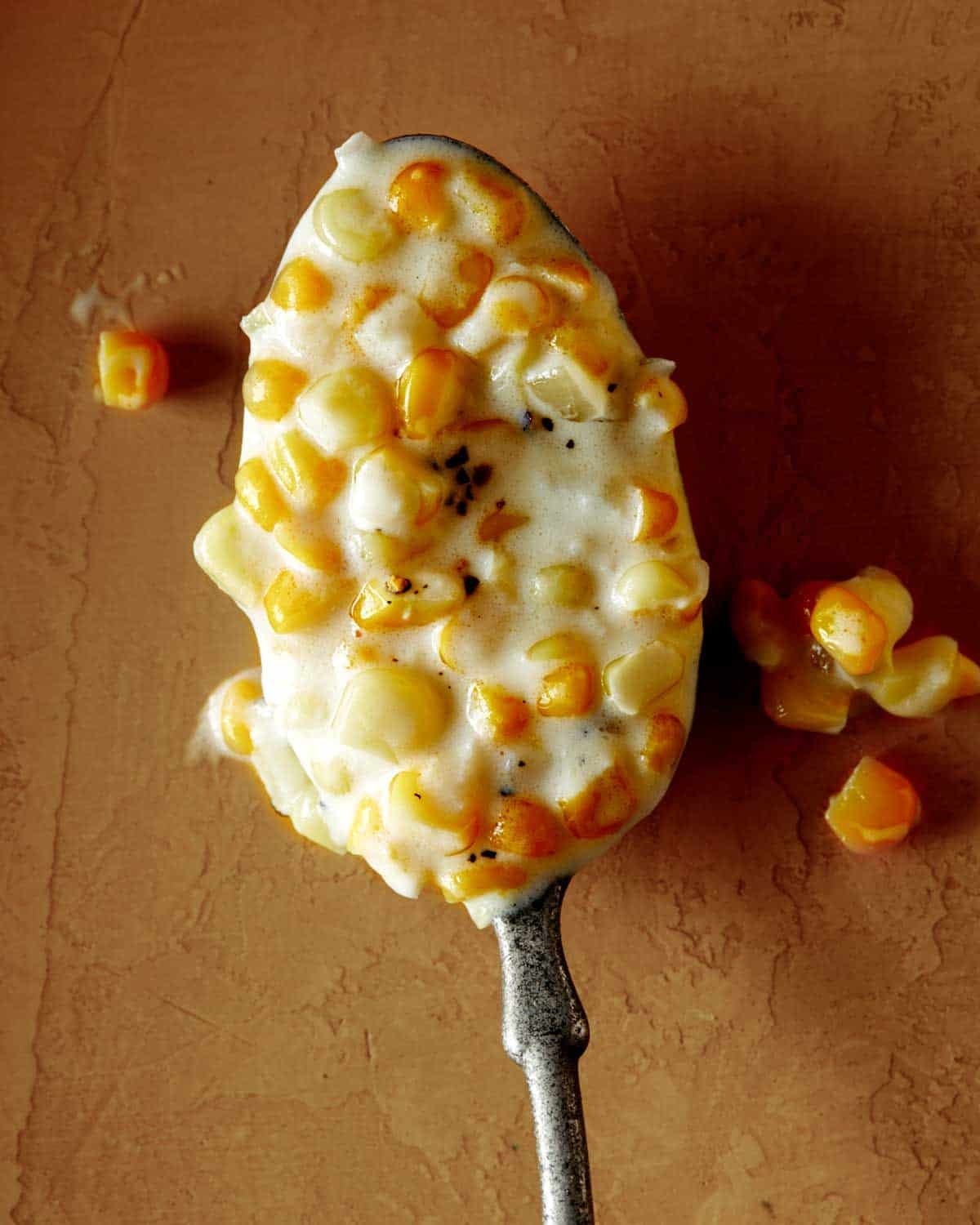 Close up on a spoon full of creamed corn on a table.