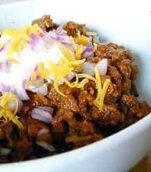 Chili in a bowl topped with sour cream, shredded cheese, and diced onion.