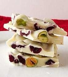 Stack of 4 pieces of pistachio and cranberry white chocolate bark on a white plate.