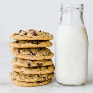 A stack of peanut butter-oatmeal chocolate chip cookies next to a glass bottle of milk.