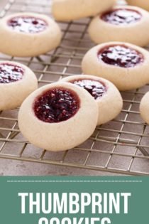 Raspberry thumbprint cookies arranged on a wire cooling rack that is set next to a glass of milk. Text overlay includes recipe name.