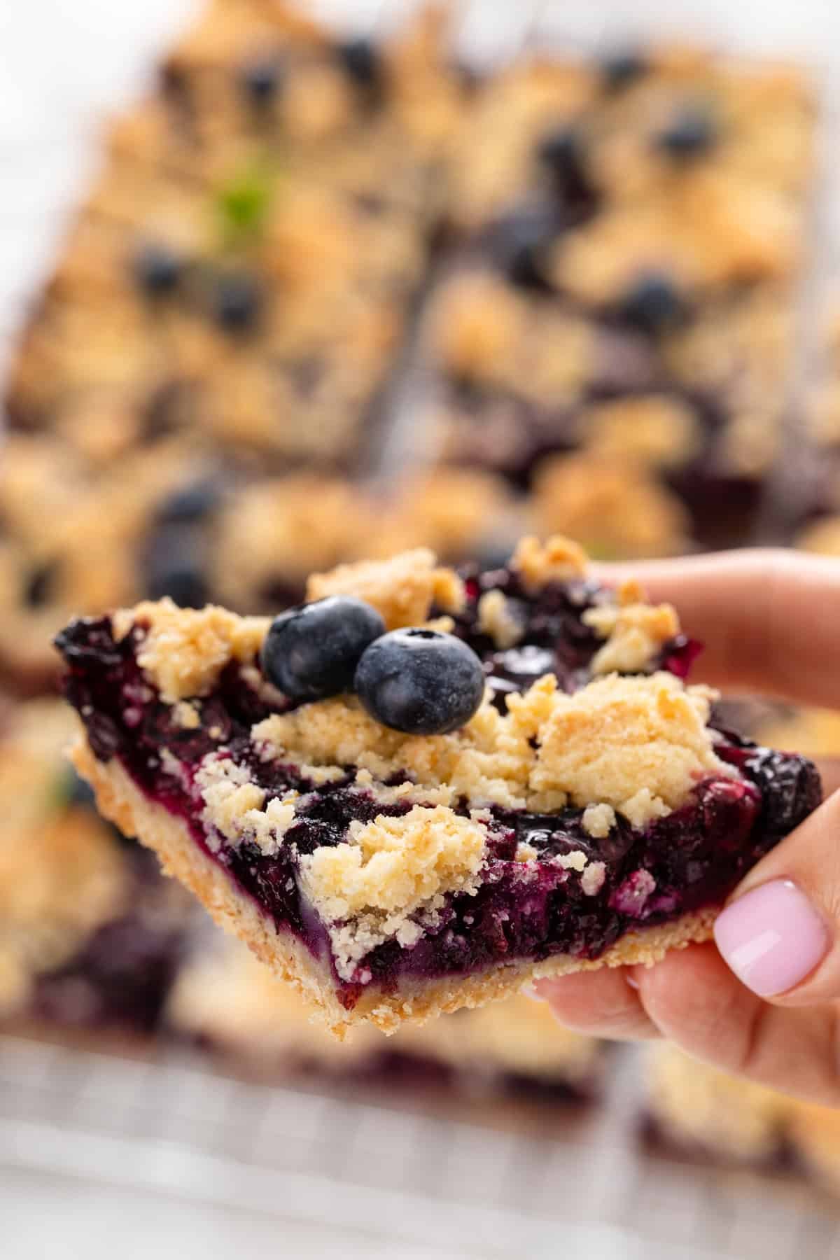 Hand holding up a blueberry crumb bar to the camera.