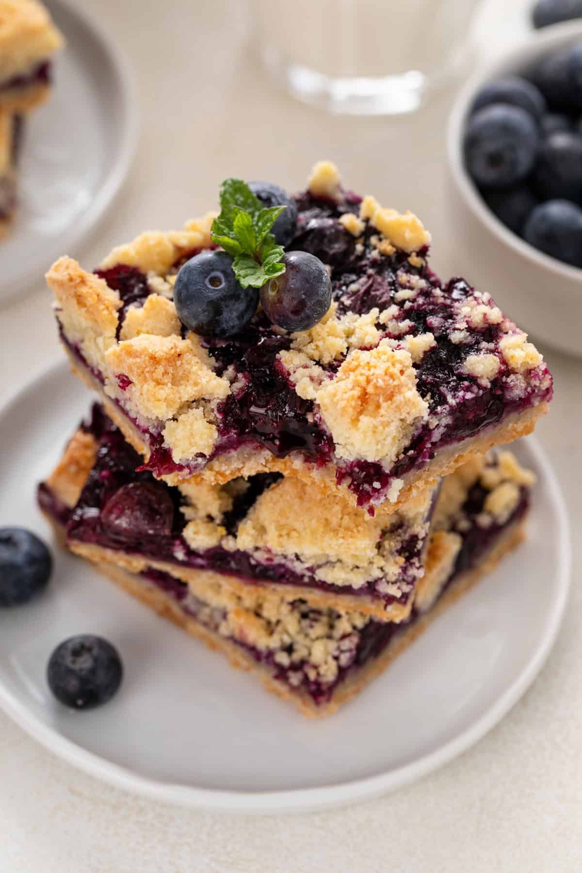 Three stacked blueberry crumb bars on a white plate with a bite taken from the top bar.