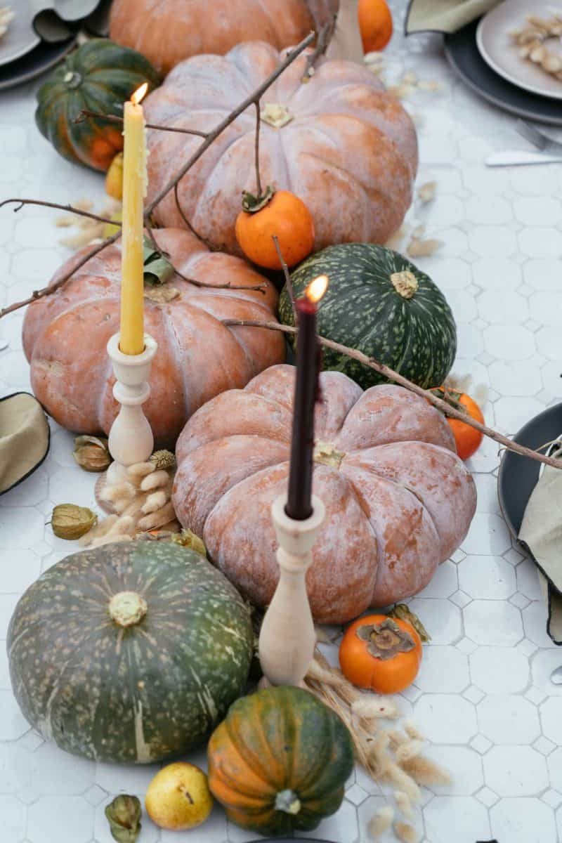 A close up of winter squash, fruits, dried bunny tails, and candles.
