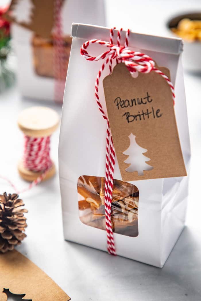 Close up of a white package filled with peanut brittle. The package is tied with red and white twine and has a tag that reads 