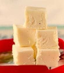 Squares of eggnog fudge stacked on a plate.