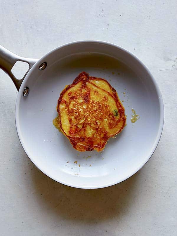 A cooked pancake in a skillet flipped to reveal with cooked and crispy side.
