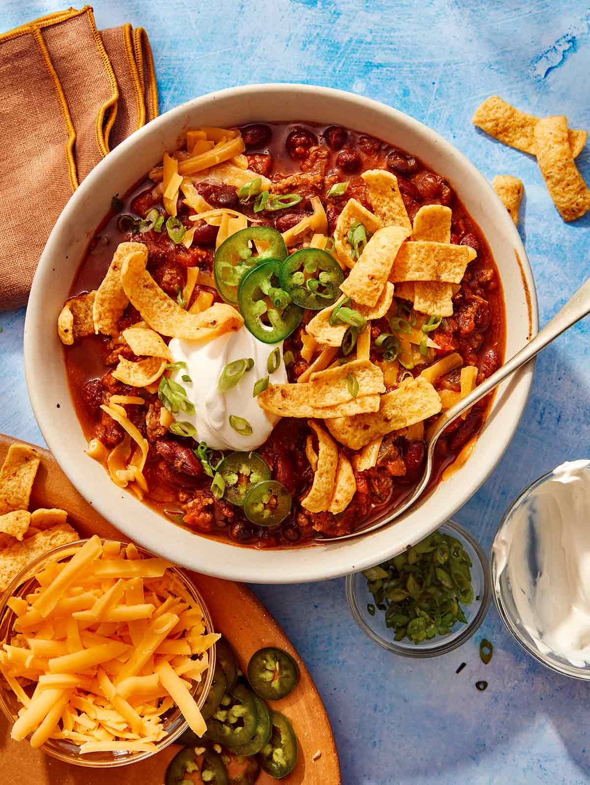 A chili recipe being served in a bowl with toppings on the side.