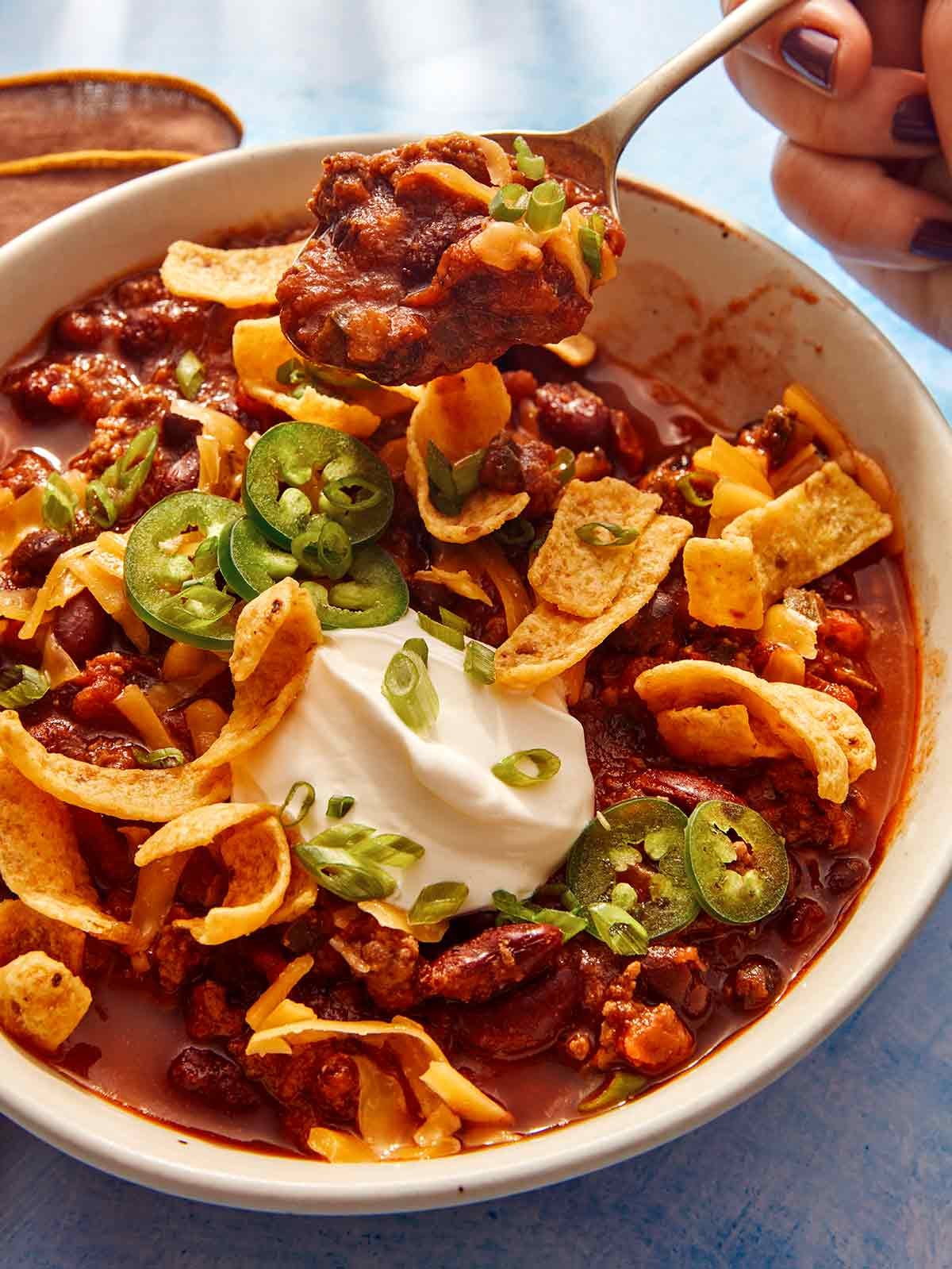 A chili recipe in a bowl with a person taking a bite out of a it with a spoon.