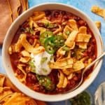 Chili in a bowl with a spoon in it and toppings on the side.