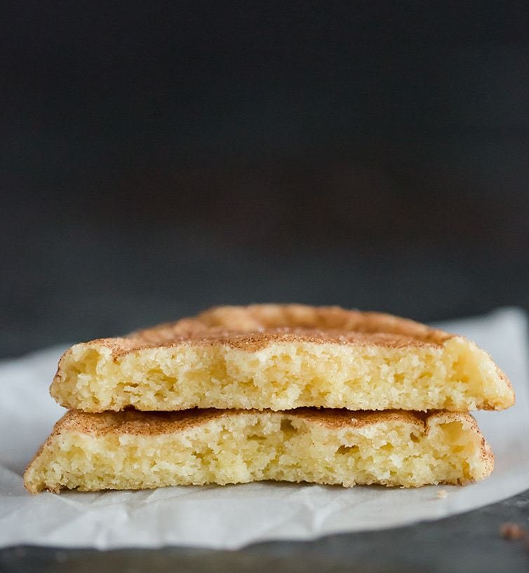 A snickerdoodle cookie broken in half on a piece of parchment paper.