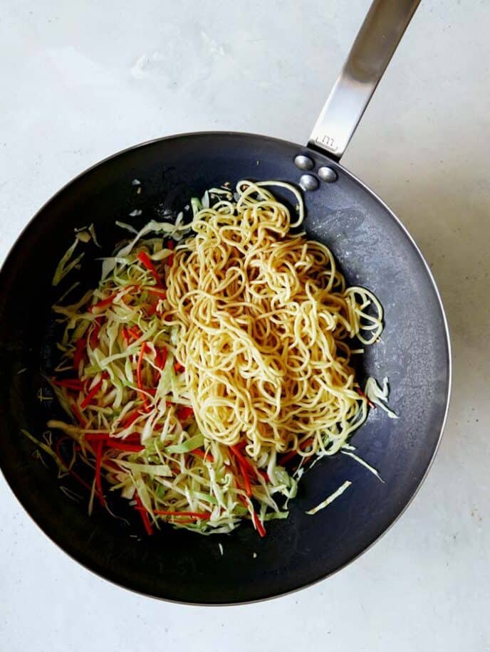 Chow Mein noodles being added to a wok of chow mein vegetables. 