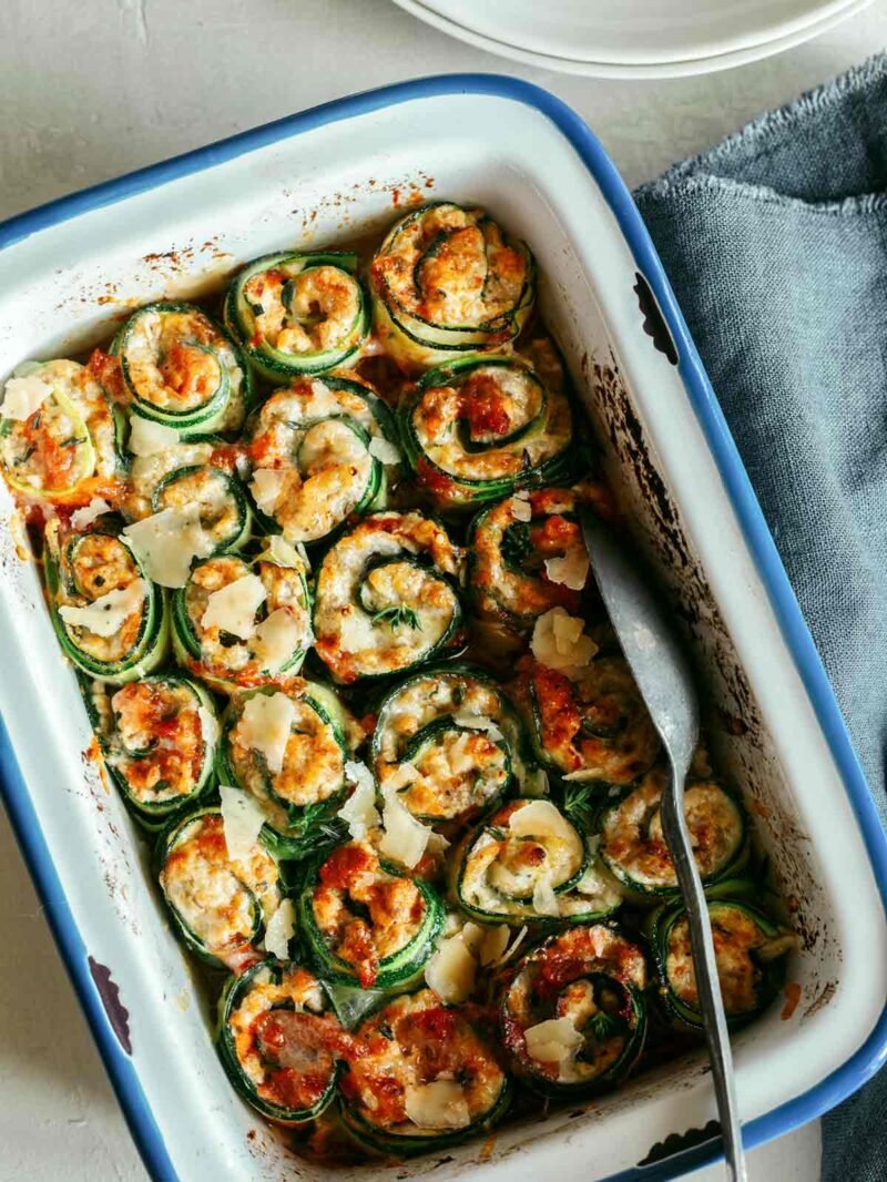 Zucchini Lasagna Rolls Ups in a baking dish with some scooped out.