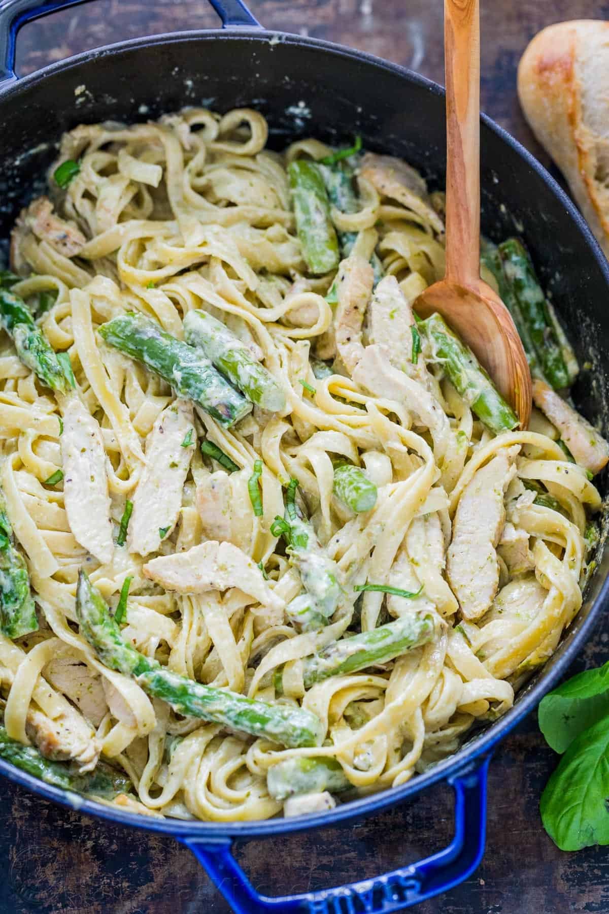 Chicken Pesto Pasta is an easy, 30-minute pasta dinner loaded with juicy chicken and asparagus. Try this crowd-pleasing pasta recipe! Pesto Chicken Pasta recipe with asparagus in a blue dish with wooden spoon.