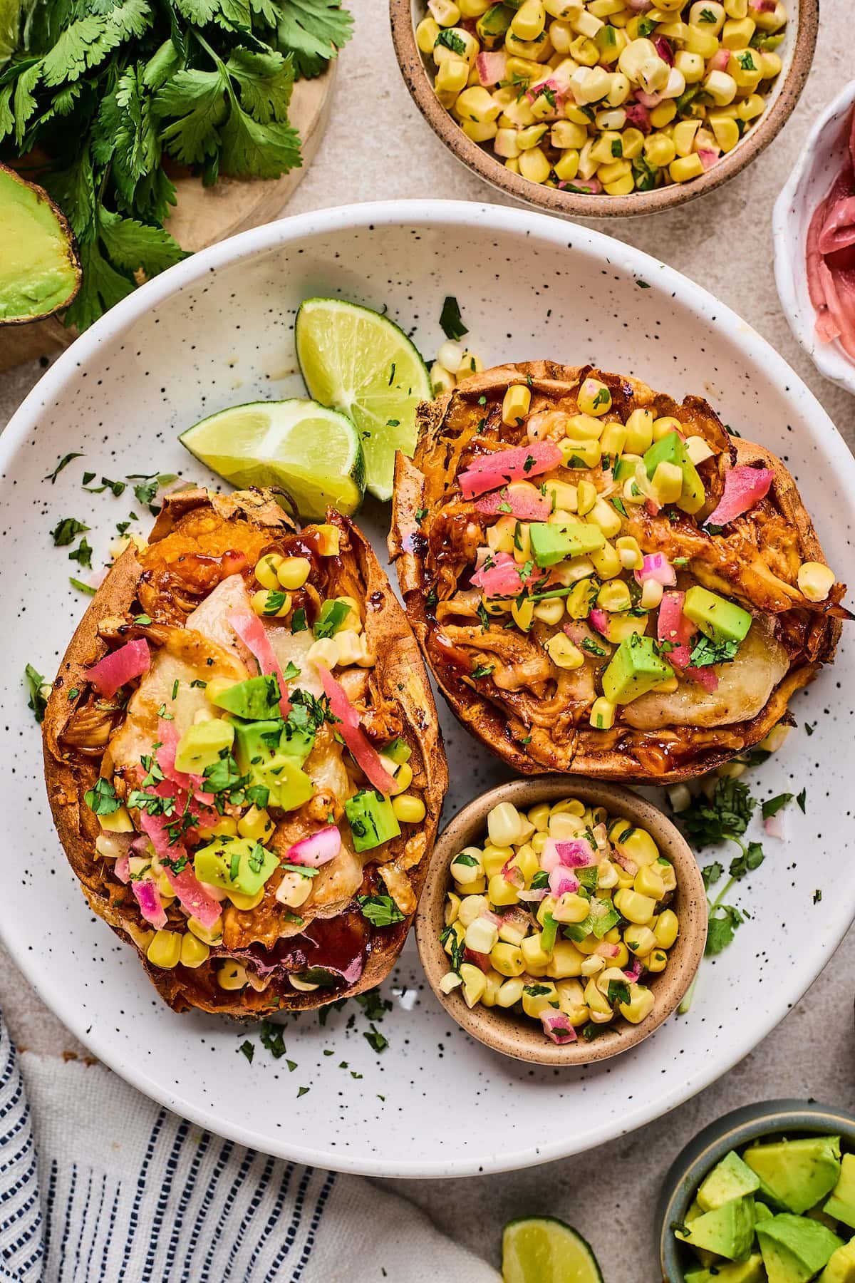 BBQ chicken stuffed sweet potatoes with corn salsa, avocado, pickled red onions, and cilantro on plate.