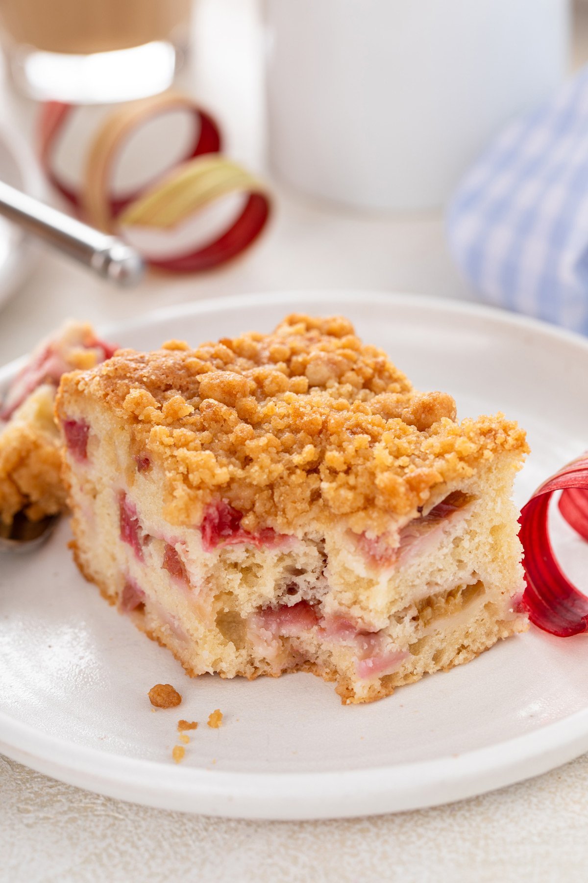 Bite taken from the corner of a piece of rhubarb streusel cake on a white plate.