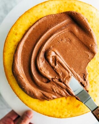 photo of chocolate fudge frosting being spread on a yellow cake