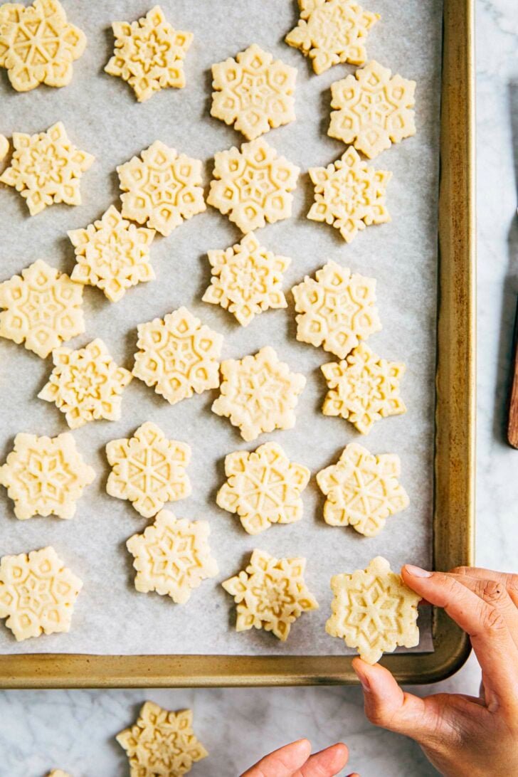 photo of michelle from hummingbird high picking up a snowflake cut out cookie from gold sheet pan