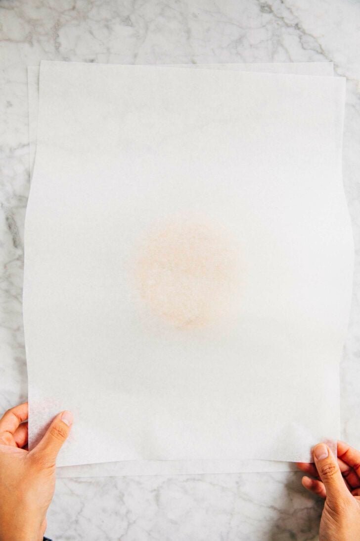 photo of michelle from hummingbird high putting a piece of parchment paper on top of the cut out sugar cookie dough