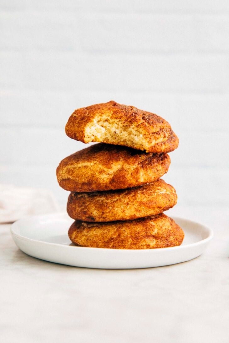 photo of four brown butter snickerdoodle cookies stacked on a small white plate