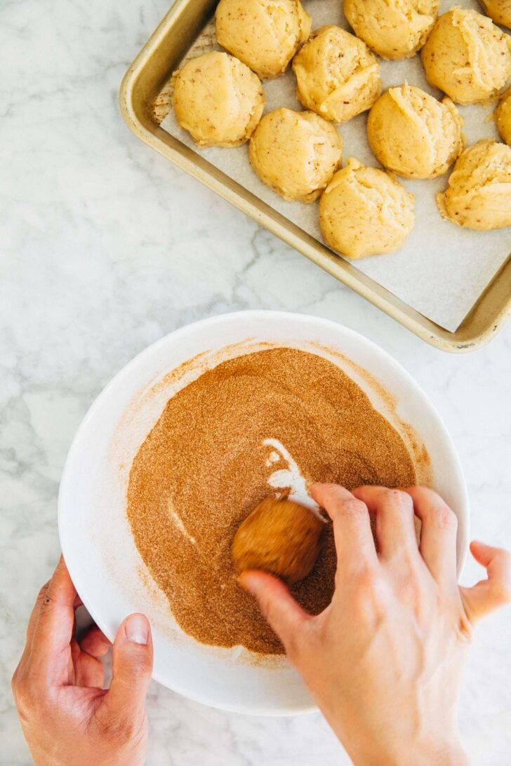 photo of michelle from hummingbird high coating a snickerdoodle cookie dough ball in cinnamon sugar