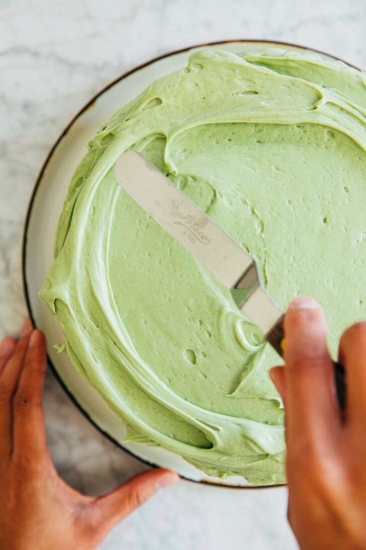 photo of michelle from hummingbird high frosting the top of the pistachio pudding layer cake