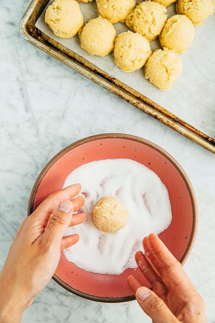 photo of a sugar cookie dough ball being tossed in the sugar topping before baking
