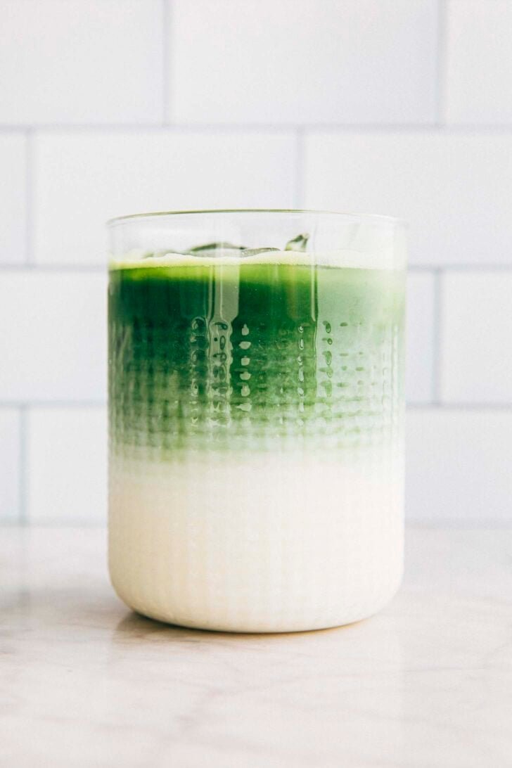 photo of layered matcha latte in a clear glass against a subway title background