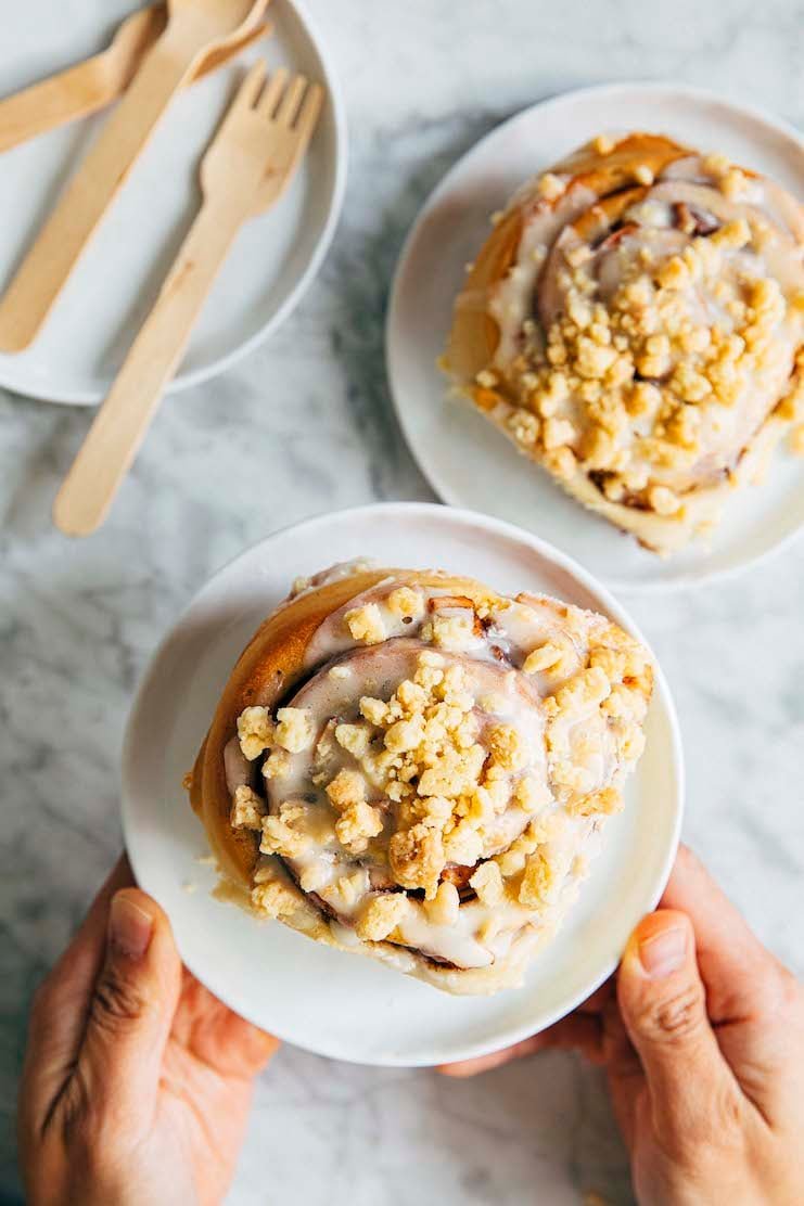 photo of hands holding up an apple pie cinnamon roll on a white plate